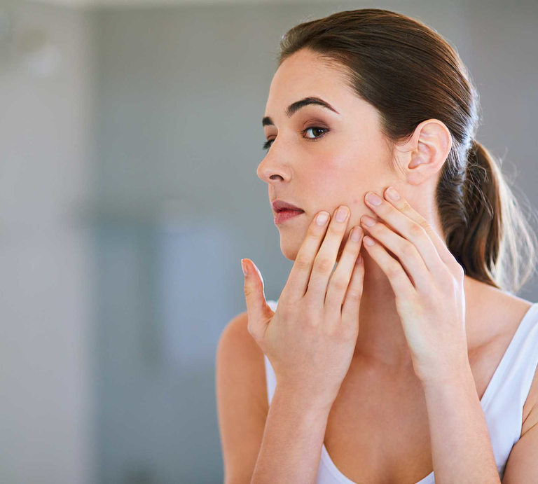 Frau schaut sich im Spiegel ihren Pickel an | © Getty Images/Peopleimages