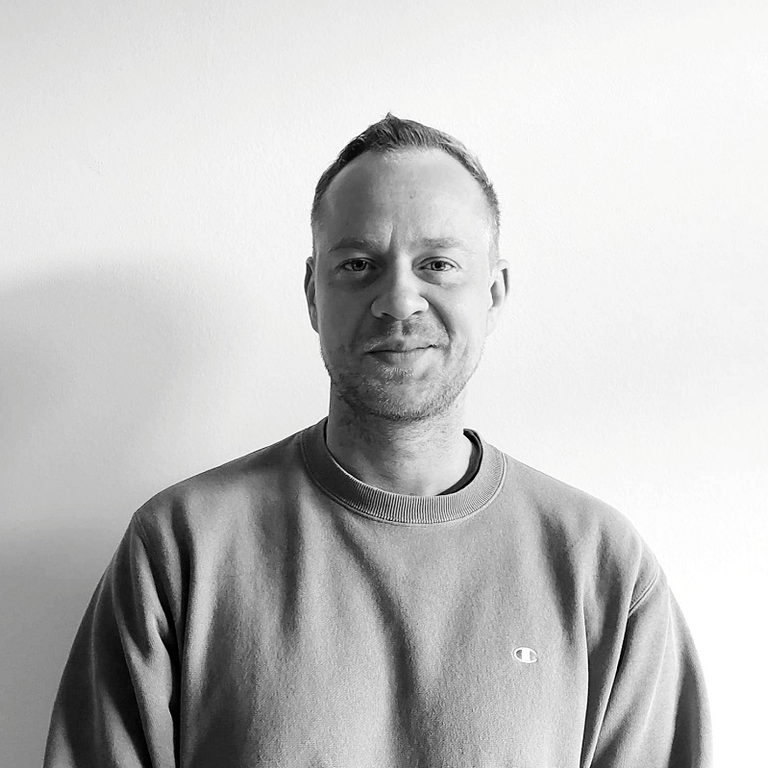 Schwarz-weiß Porträt eines lächelnden Mannes mit kurzem Haar und einem lässigen Sweatshirt, vor einem hellen Hintergrund, der eine entspannte und freundliche Ausstrahlung vermittelt. | © privat