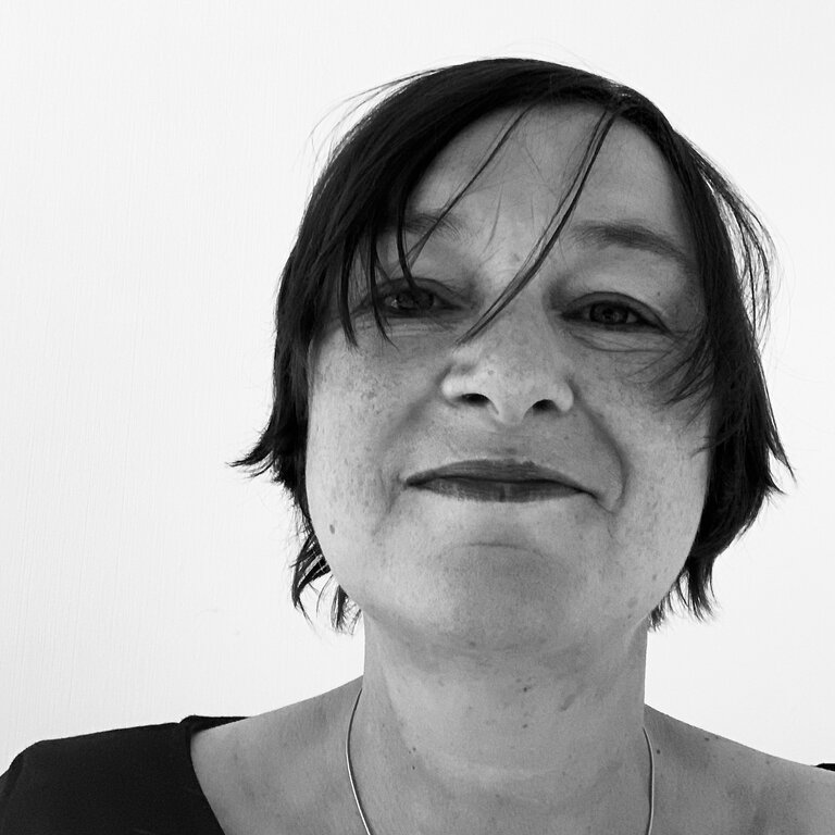 Schwarz-weiß Porträtfoto einer lächelnden Frau mit kurzen dunklen Haaren und einem schlichten Oberteil. | © privat