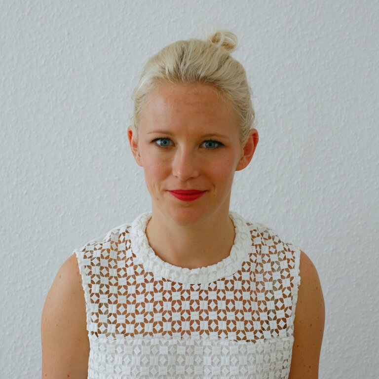 Blonde Frau mit rotem Lippenstift in weißem Shirt lächelt in die Kamera.  | © privat