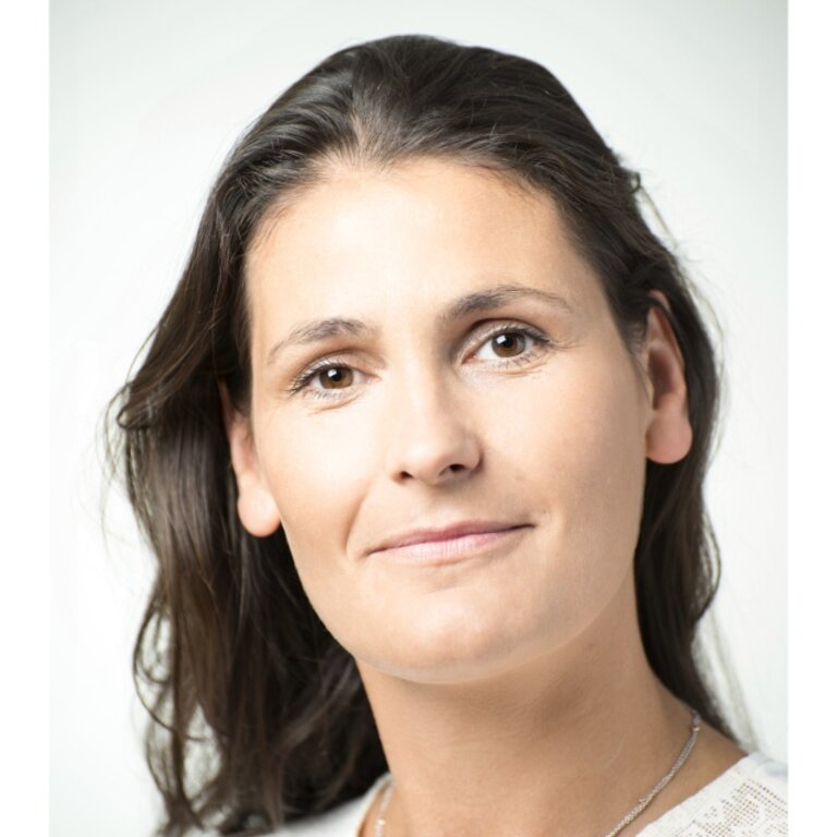 Das Bild zeigt eine Frau mit einem nachdenklichen und ruhigen Gesichtsausdruck. Sie hat lange, dunkle Haare und trägt ein weißes Oberteil mit einer feinen Halskette. Ihr Blick ist leicht nach oben gerichtet und sie scheint in die Ferne zu schauen. Der Hintergrund ist schlicht und hell, was die Aufmerksamkeit auf ihr Gesicht lenkt. | © privat