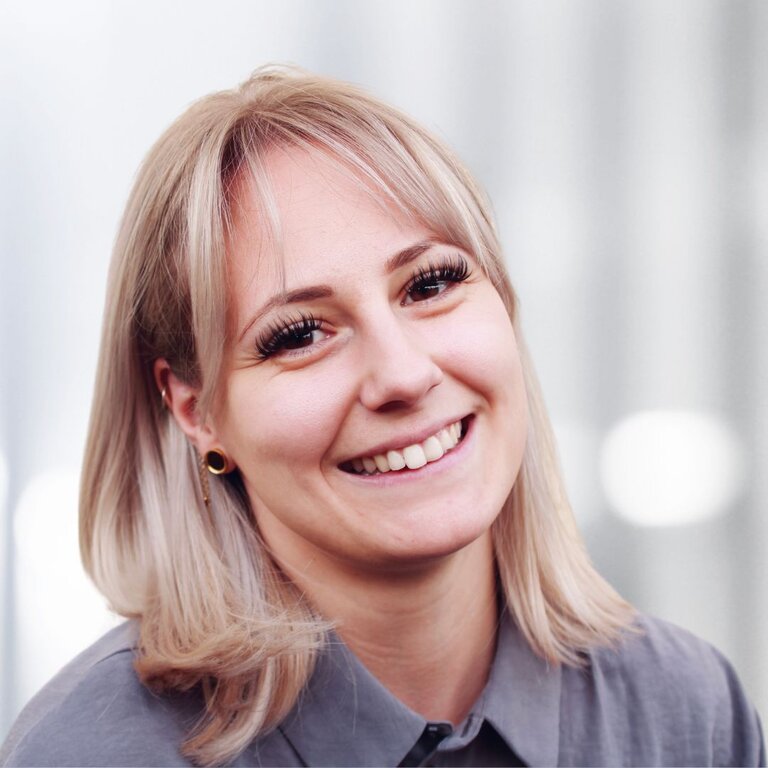 Das Bild zeigt eine lächelnde Frau, die direkt in die Kamera blickt. Sie hat blonde Haare, die in einem mittellangen Schnitt mit leichter Welle gestylt sind. | © privat