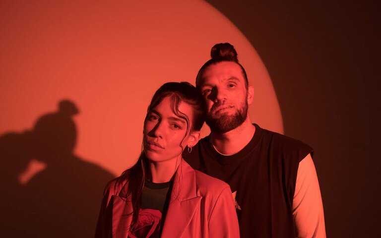 Alina Süggeler und  Andi Weizel von Frida Gold vor rot ausgeleuchtetem Hintergrund. | © Fabian Süggeler