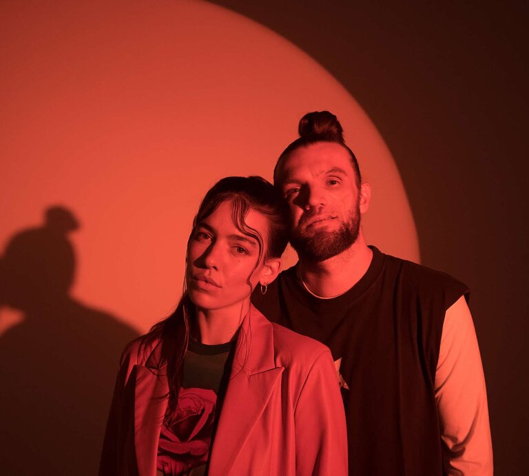 Alina Süggeler und  Andi Weizel von Frida Gold vor rot ausgeleuchtetem Hintergrund. | © Fabian Süggeler
