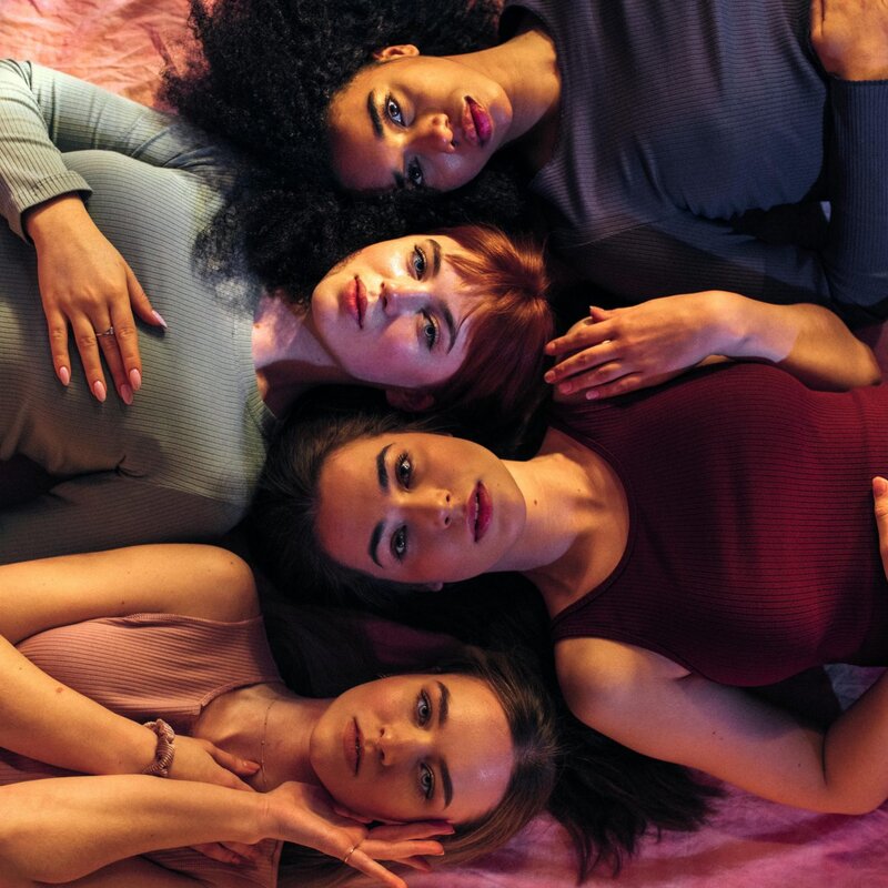 Vier weiblich gelesene Personen liegen auf dem Rücken und blicken aus der Vogelperspektive direkt in die Kamera. | ©  Pexels | Kool Shooters