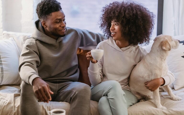 Bild von einem Mann und einer Frau, die auf einer Couch sitzen. Die Frau hat einen Hund im Arm. | © Andres Ayrton | Pexels