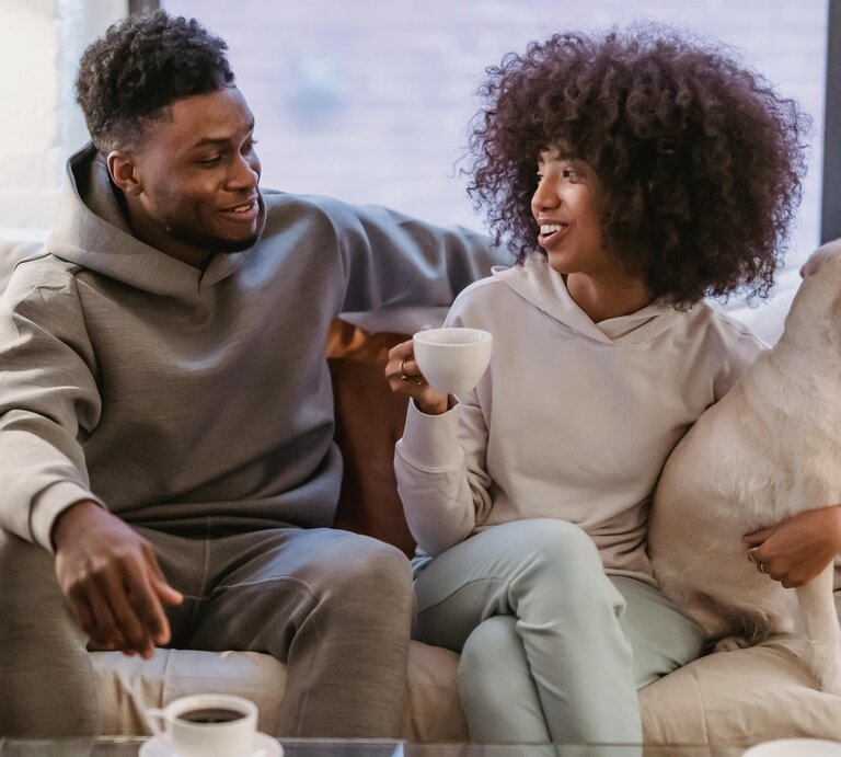 Bild von einem Mann und einer Frau, die auf einer Couch sitzen. Die Frau hat einen Hund im Arm. | © Andres Ayrton | Pexels