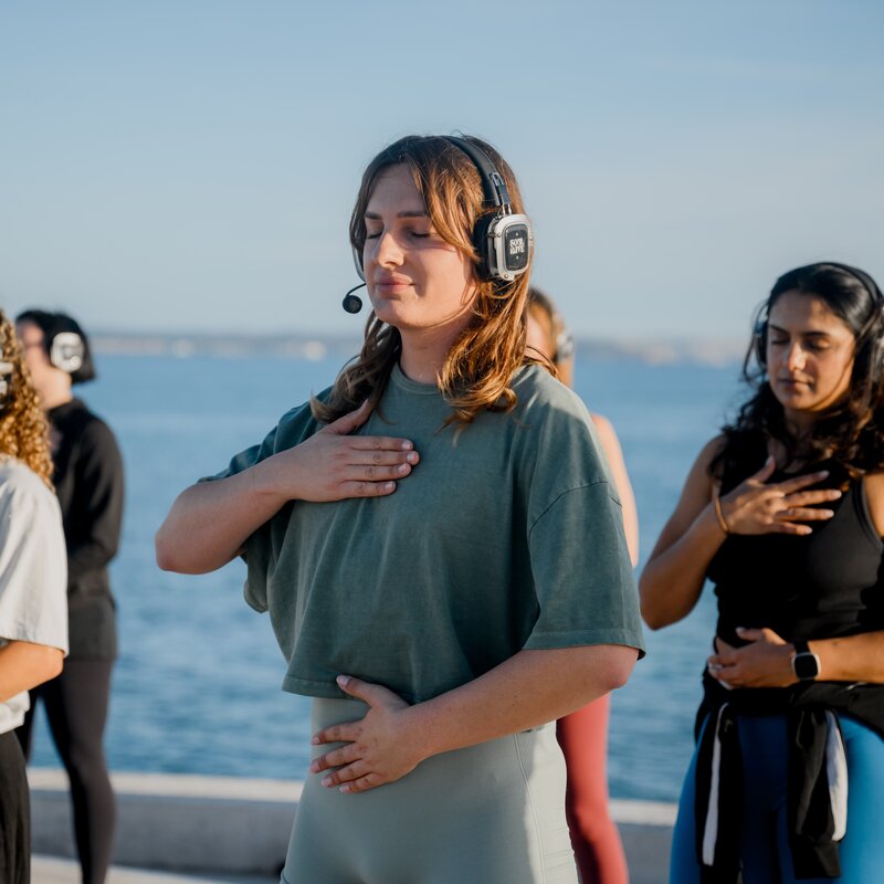 Leni Bolt steht unter anderen Menschen mit Silent Disco Kopfhörern und Sportklamotten. Alle haben ihre Augen geschlossen und haben eine Hand auf dem Herzen. | © Leni Bolt