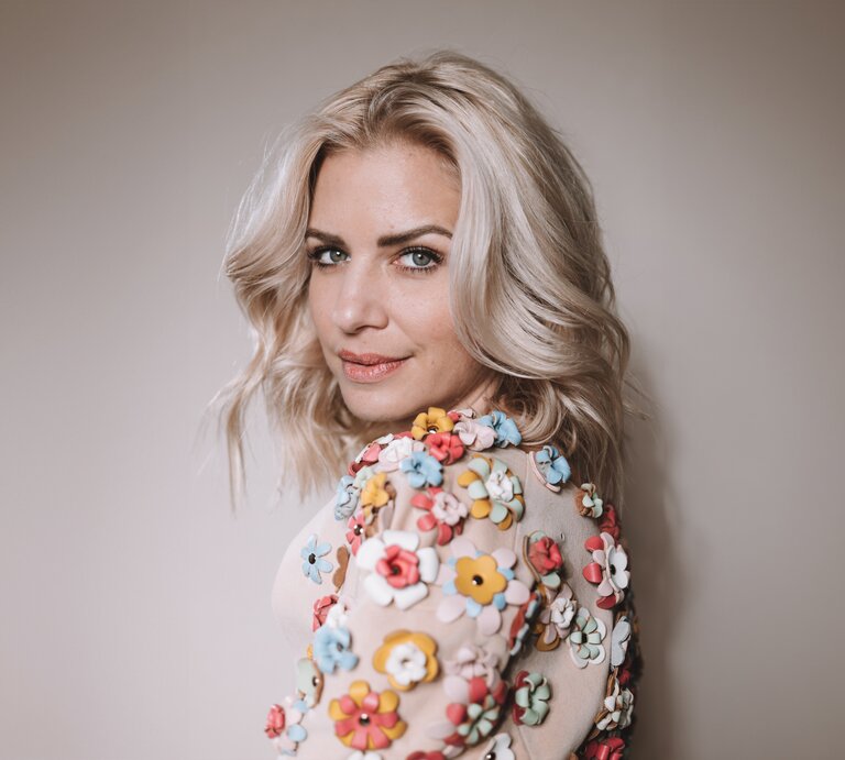 Susan Sideropoulos steht vor einem Fotowand und lächelt | © Liesa Fuchs