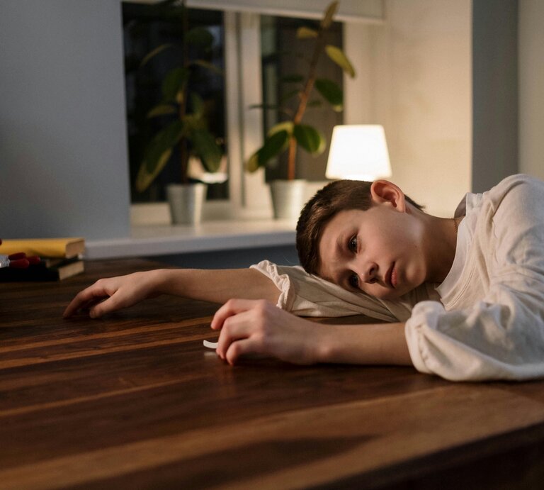 Kind, weißes Hemd, legt kopf traurig auf den Tisch, blickt neutral in die Ferne.  | © Cottonbro | Pexels