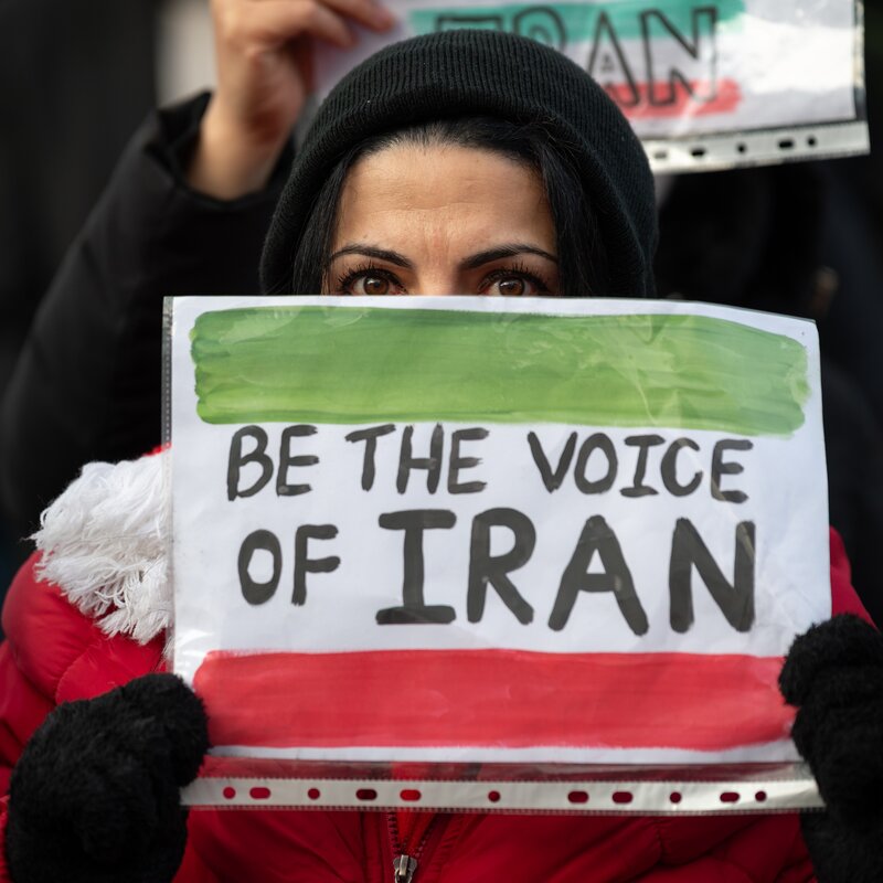 Foto einer protestierenden Frau, auf deren Schild "Be the voice of Iran" geschrieben steht. | © Sopa Images, Getty Images | Aufmerksamkeit für die Situation im Iran soll Druck auf die Machthaber ausüben.
