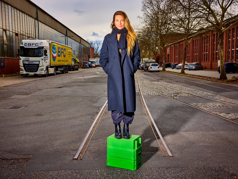 Dr. Martyna Linartas steht auf einer knallgrünen Holzkiste mitten in einem Industriegebiet.  | © Norman Konrad | Dr. Martyna Linartas forscht zu Vermögen.