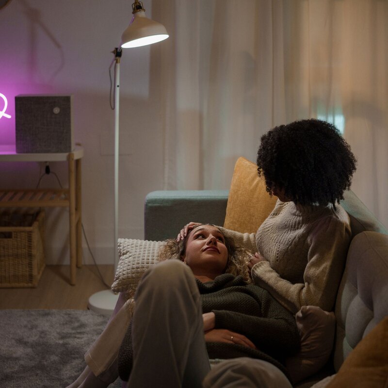Zwei Personen sitzen auf einem Sofa bei leicht gedimmtem Licht. Die eine Person streichelt der anderen Person sanft über den Kopf. | © Getty Images/Ivan Rodriguez Alba