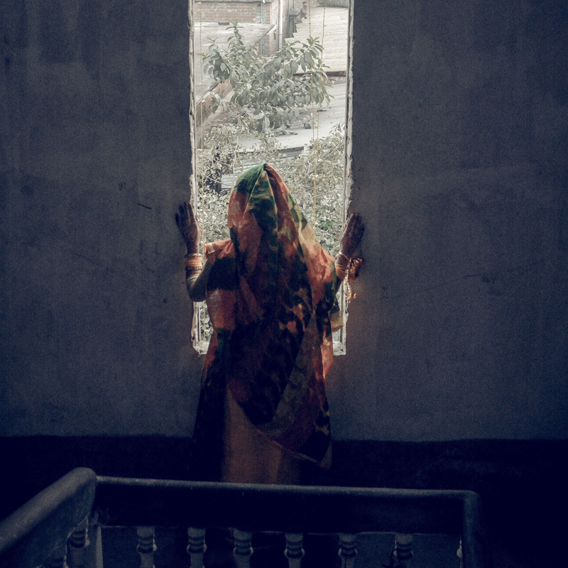 Eine Frau in traditioneller Kleidung steht in einem unheimlichen, verlassenen Treppenhaus, eingerahmt von einem Fenster. | ©  Sadman Chowdhury | Pixels