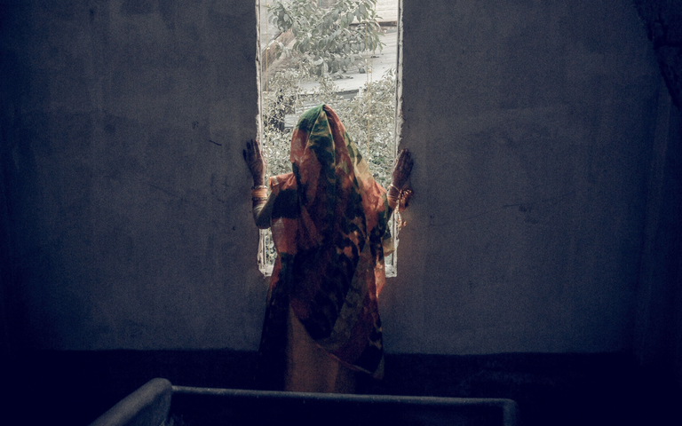 Eine Frau in traditioneller Kleidung steht in einem unheimlichen, verlassenen Treppenhaus, eingerahmt von einem Fenster. | ©  Sadman Chowdhury | Pixels
