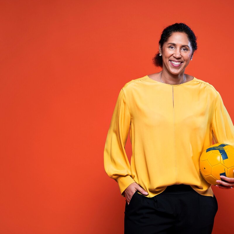 Bild von Steffi Jones in gelber Bluse mit einem gelben Ball vor rotem Hintergrund | © Steffi Jones