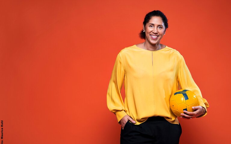 Bild von Steffi Jones in gelber Bluse mit einem gelben Ball vor rotem Hintergrund | © Steffi Jones