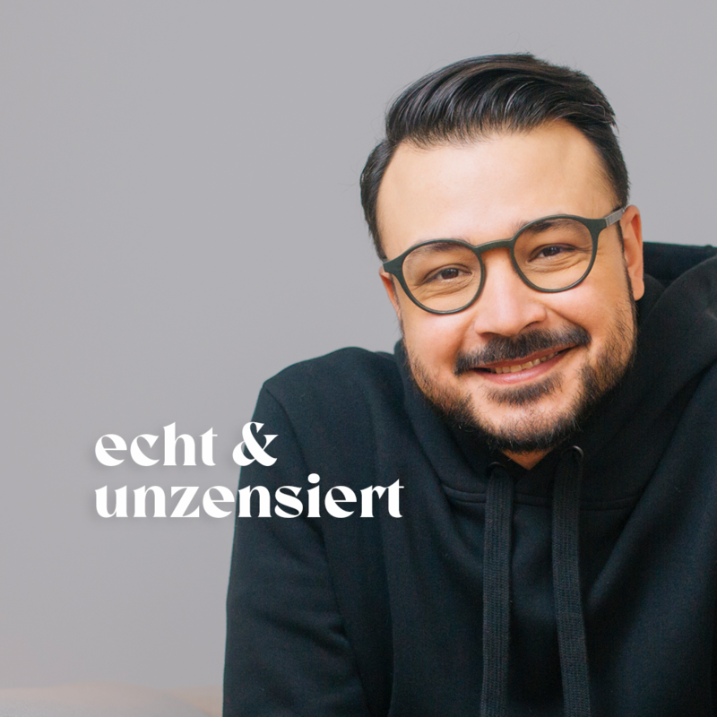 Psychologe Umut Özdemir sitzt vor einer weißen Fotowand und lächelt. | © Credit: Mehran Djojan