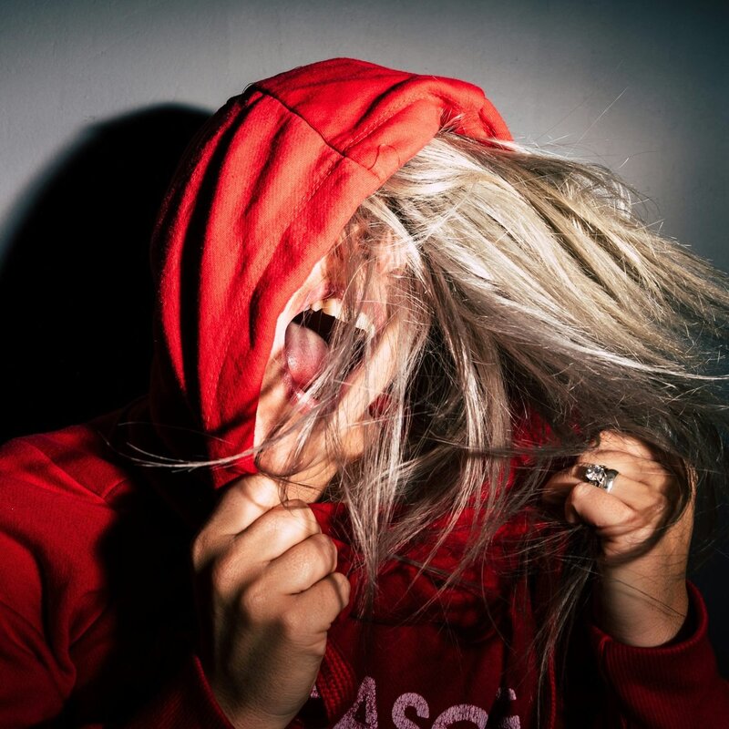 Eine Frau in rotem Kapuzenpulli schreit wütend und ballt sie Hände zu Fäusten. | © Bild: Jan Kopriva | Unsplash