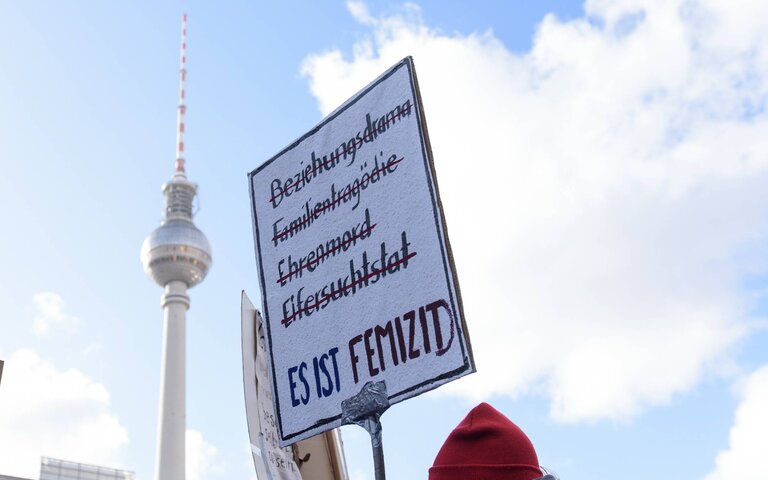 Demonstrationsschild: Es ist Femizid. Hintergrund: Blauter Himmel und Fernsehturm in Berlin | © Foto: Christian Spicker | IMAGO 