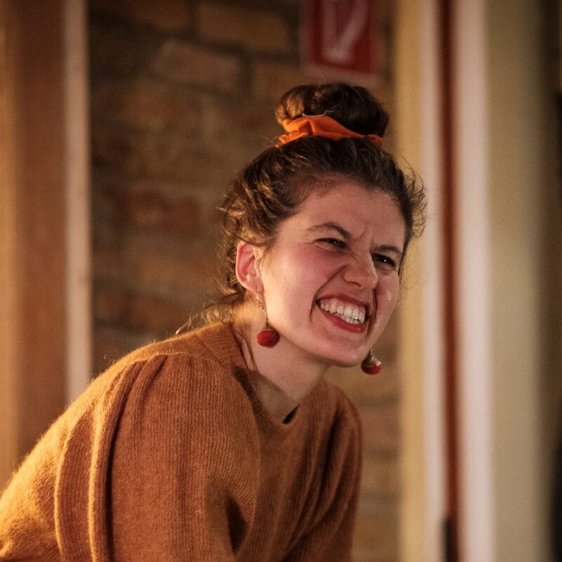 Käthe spielt am Klavier und reißt ihr Publikum mit – Hintergrund bräunlich. Und Käthe trägt ein beiges Kleid, ist vertieft in die Musik.