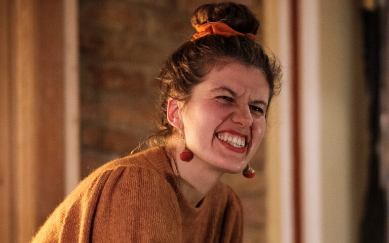 Käthe spielt am Klavier und reißt ihr Publikum mit – Hintergrund bräunlich. Und Käthe trägt ein beiges Kleid, ist vertieft in die Musik.