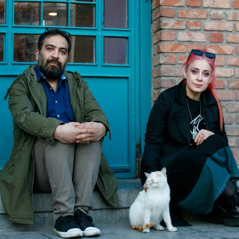 Das Foto zeigt einen Mann und eine Frau, die auf einer Stufe vor eine Tür sitzen. | © Behtash Sanaeeha und Maryam Moghadam |  Foto: Mehdi Hasani 