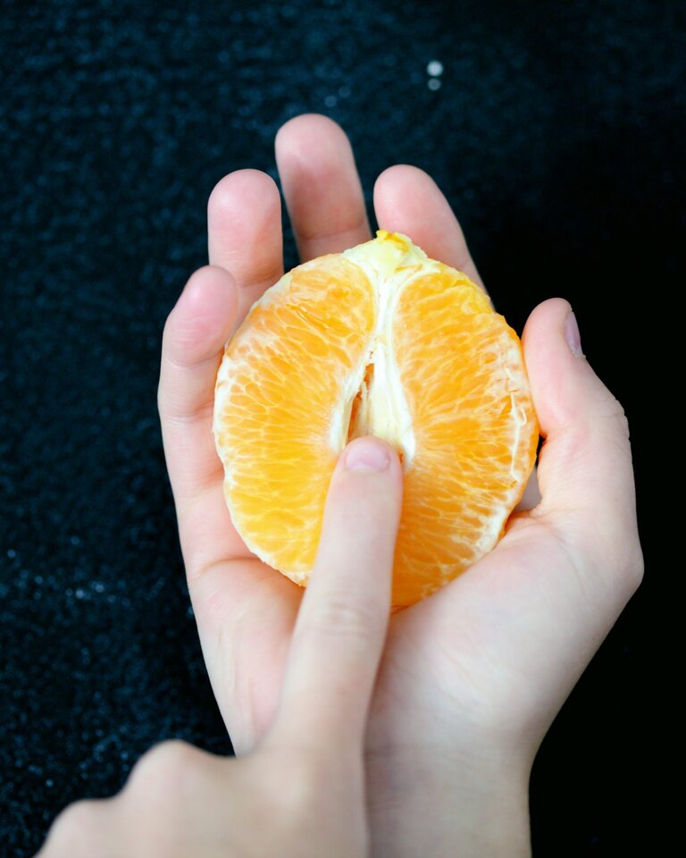 Eine Hand hält eine halbe, geschälte Orange, die eine Vulva symbolisieren soll. | © Foto: Sharon McCutcheon/Unsplash

